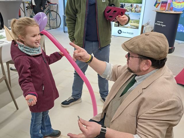 Fred Funke kniet vor einem kleinen Mädchen und zaubert mit einem Luftballon