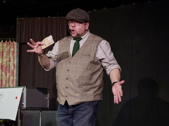 Fred Funke in Weste und Schiebermütze auf der Bühne