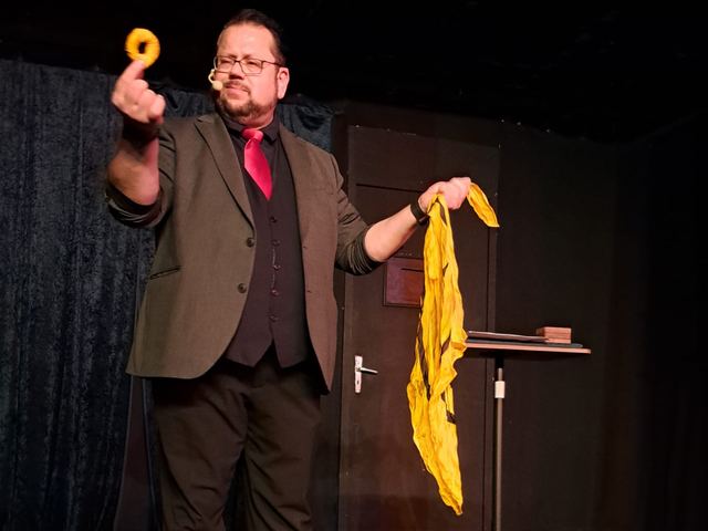 Fred Funke mit gelbem Tuch und Ring auf einer dunklen Bühne