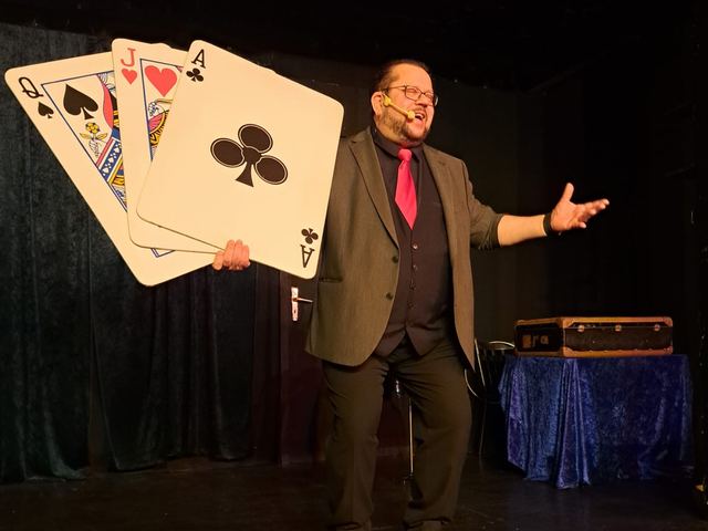 Fred Funke fächert Riesenspielkarten auf einer dunklen Bühne auf