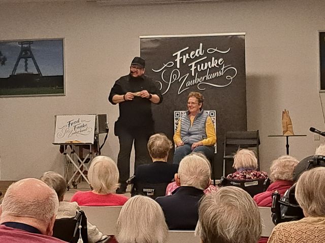 Fred Funke mit einer Zuschauerin auf der Bühne vor Seniorinnen und Senioren